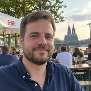 Porträt von Jannik Behrendt, Mann Mitte dreißig mit kurzem Bart und dunkelblauem Hemd