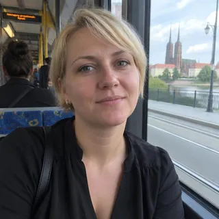 Portret Beaty Zawadzkiej, kobiety po trzydziestce z krótkimi jasnymi włosami w ciemnej bluzce